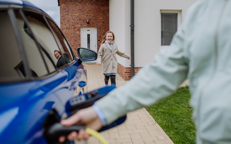 Man charging electric car as daughter runs along